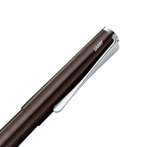 The Lamy studio dark brown is a Special Edition 2022. The LAMY studio elegantly shows just how close design and art can be. This premium writing instrument seamlessly fuses its individual elements with its convex cylindrical form while simultaneously foregoing all unnecessary embellishments. The propeller-shaped, seemingly twisted clip counters the objective elegance of the LAMY studio with an innovative design accent. This 2022 special edition has a dark brown body with a glossy finish and subtle shimmer. It is equipped with a high gloss chrome grip and clip. This Roller Ball Pen comes with a large capacity LAMY M 63 refill so you can get started writing right away. The final result is an indulgent writing experience you will revel in each time pen touches paper. The studio is also an ideal gift for someone particularly special. Dark Brown  Made from lacquer finish metal body with propeller-shaped clip Snap Cap with chrome plated trim Material: Metal Rollerball pen has a medium nib with smooth-writing. Roller Ball pen is used with a large capacity LAMY M 63 refill. Roller Ball pen comes with a Original brand packaging. Brand Origin: Germany